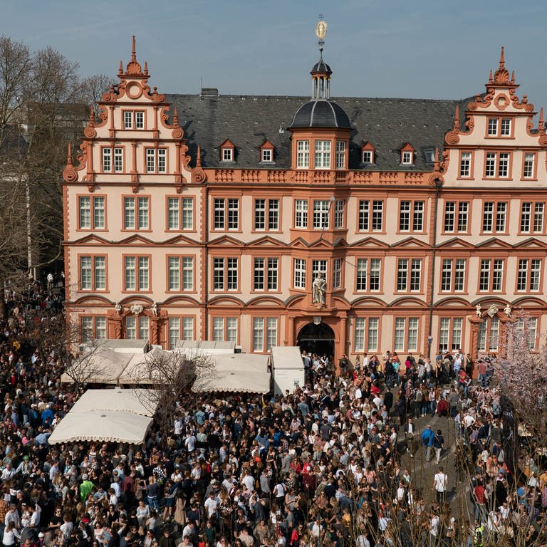 Luftaufnahme vom Marktfrühstück in Mainz. Der Weinausschank befindet sich vor dem Gutenberg-Museum.Hunderte Menschen stehen davor und trinken ein Glas Wein oder Saft.mainz