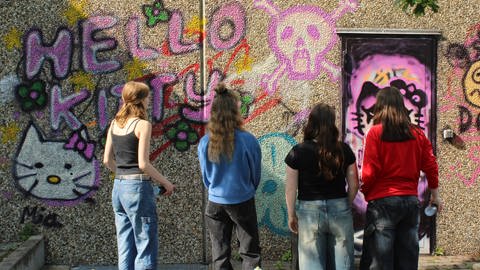 Vier junge Frauen schauen sich das mit Graffiti besprühte alte Hallenbad in Oppenheim an.
