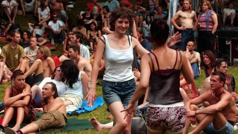 Das Open Ohr Festival in Mainz im  Jahr 2003. Zwei Frauen tanzen auf einer Wiese, im Hintergrund sitzen Menschen. (Quelle: IMAGO) 