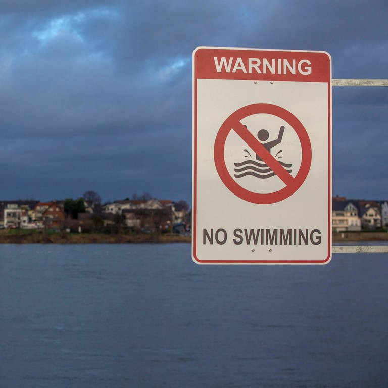 Ein Warnschild no swimming steht am Rheinufer: Polizei in Mainz: Schwimmen im Rhein ist lebensgefährlich (Foto:IMAGO).