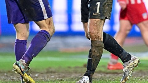 Zu sehen sind die Beine zweier Fußballer im Regen. Bei Amateur-Fußballspielen kommt es immer wieder zu Gewalt.