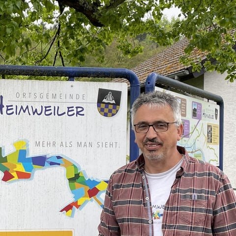 Ortsbürgermeister Setz steht vor einem Schild mit dem Logo von Heimweiler