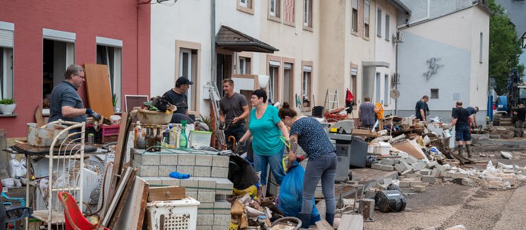 Menschen räumen im Stadtteil Ehrang die Schäden nach dem Hochwasser der Kyll auf. Zahlreiche Häuser im Ort waren betroffen, Bewohner mussten evakuiert werden. (Foto: dpa Bildfunk, picture alliance/dpa | Harald Tittel)