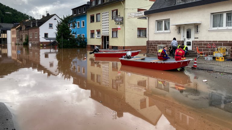 Straße in Kordel (RLP), die nach dem Hochwasser 2021 unter Wasser steht. Am Wasserrand befinden sich drei Boote der Feuerwehr und zwei Einsatzkräfte (Foto: SWR, Eva Lamby-Schmitt)