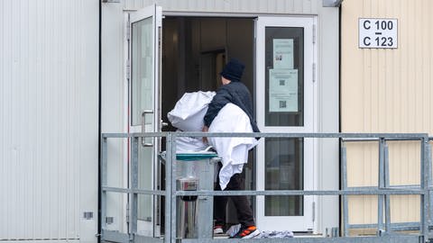 Ein Mann geht mit Bettzeug in einen Container mit Wohnbereichen in der Aufnahmeeinrichtung für Asylbegehrende (AfA) in Trier. (Foto: dpa Bildfunk, picture alliance/dpa | Harald Tittel)