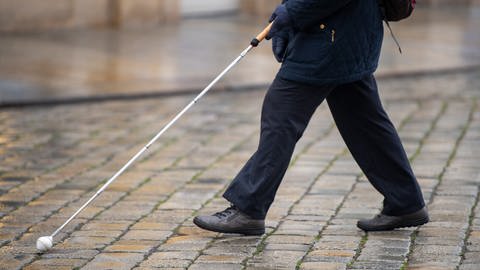 Eine blinde Person geht mit ihrem Blindenstock eine Straße entlang. (Foto: dpa Bildfunk, Picture Alliance)