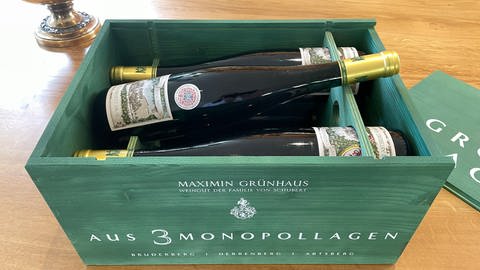Eine grüne Holzkiste mit sechs Flaschen Wein von Maximin Grünhaus. Auf einer der Flaschen ist ein Siegel angebracht. Darauf eine Krone und die Daten der Krönung von König Charles: 6. Mai 2023.  (Foto: SWR)