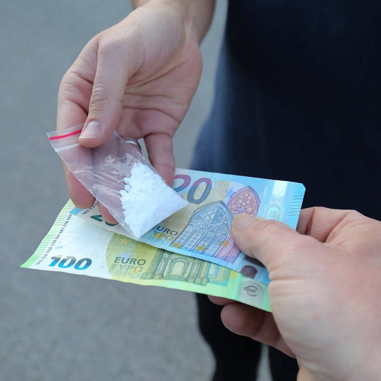 Ein Mann gibt einem anderen Mann Geld und erhält dafür Drogen in einem Tütchen (Symbolbild). (Foto: IMAGO, Daniel Scharinger)