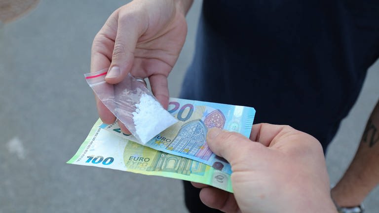 Ein Mann gibt einem anderen Mann Geld und erhält dafür Drogen in einem Tütchen (Symbolbild). (Foto: IMAGO, Daniel Scharinger)