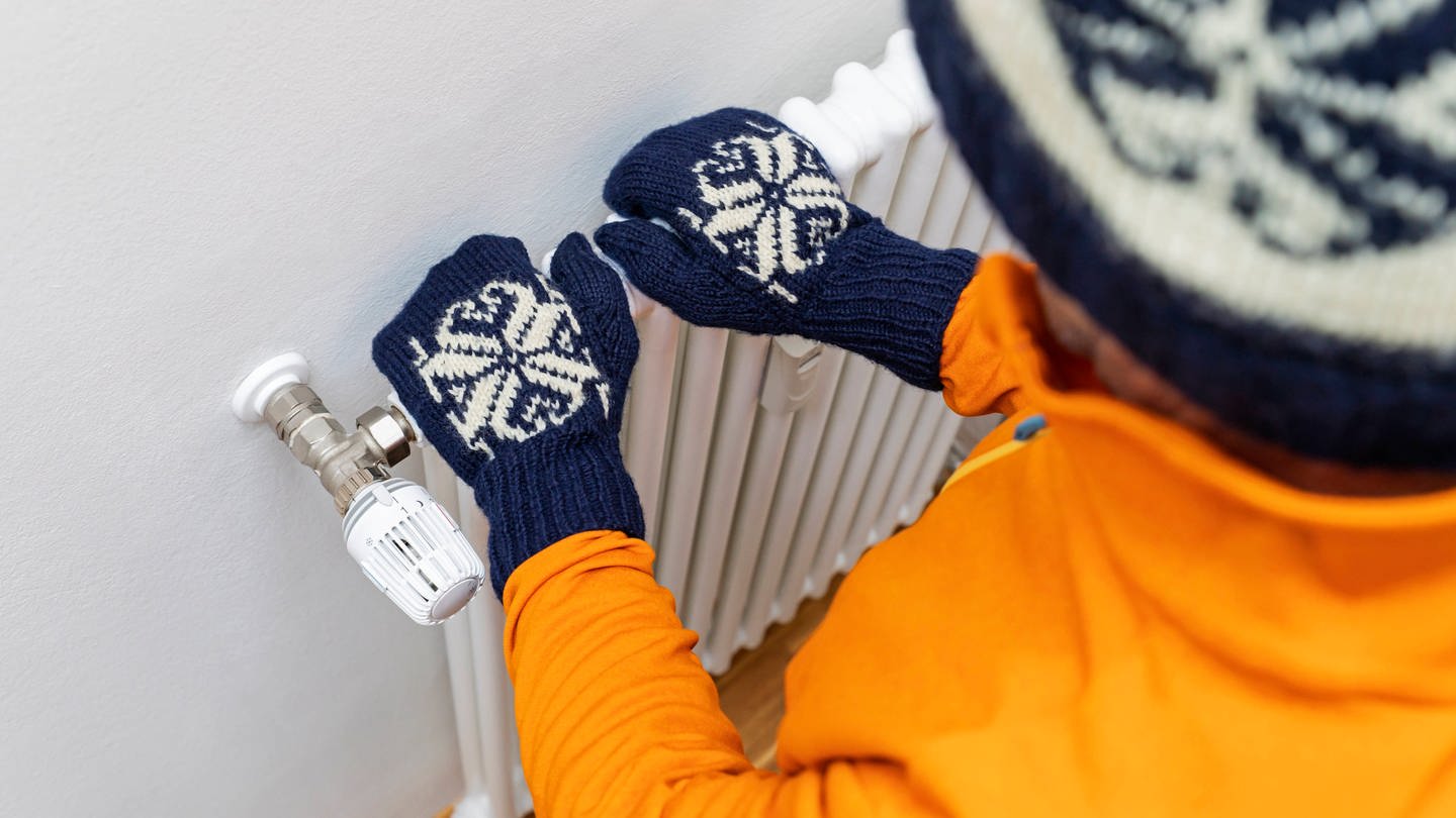 Ein Mann mit Handschuhen und Mütze fasst eine kalte Heizung an. (Foto: IMAGO, IMAGO / Westend61)