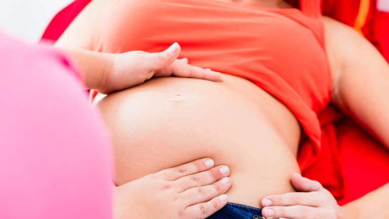 Eine Hebamme tastet den Bauch einer schwangeren Frau ab. (Foto: IMAGO, YAY Images)