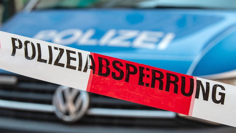 Ein Band mit der Aufschrift "Polizeiabsperrung" ist vor einem Polizeiauto gespannt. Die Kriminalpolizei ermittelt aktuell nach dem Fund von zwei Leichen in Bitburg. Bei den Toten handelt es sich wohl um ein geschiedenes Ehepaar. (Foto: dpa Bildfunk, Swen Pförtner)