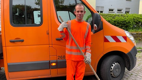 Patrick steht in seiner orangenen Arbeitskleidung vor dem Wagen der Stadt Trier.  (Foto: SWR)
