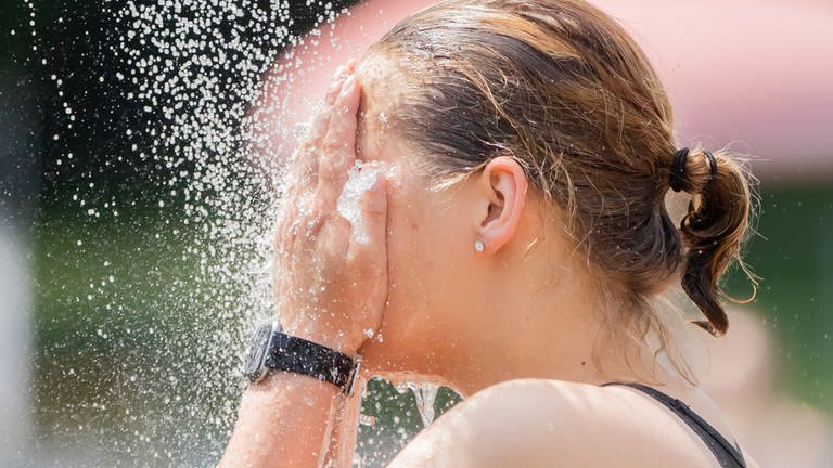 Frau kühlt sich das Gesicht mit Wasser ab. (Foto: dpa Bildfunk, Picture Alliance)