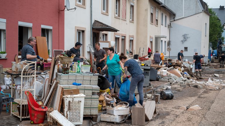 Menschen räumen im Stadtteil Ehrang die Schäden nach dem Hochwasser der Kyll auf. Zahlreiche Häuser im Ort waren betroffen, Bewohner mussten evakuiert werden.