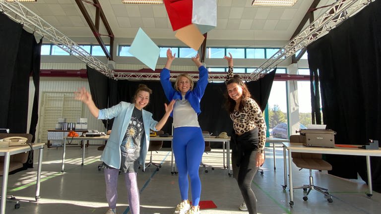 Die drei Hauptdarstellerinnen des diesjährigen Musicals der Theaterfestspiele Vulkaneifel "9 to 5" werfen Kladden in die Luft. (Foto: SWR, Anna-Carina Blessmann)