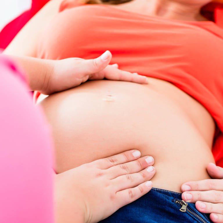 Eine Hebamme tastet den Bauch einer schwangeren Frau ab.