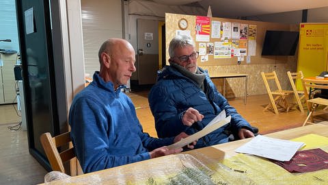 Die beiden Betroffenen Reinholf Neisius und Michael Naber sitzen am Tisch im Infozelt in Trier-Ehrang. (Foto: SWR)