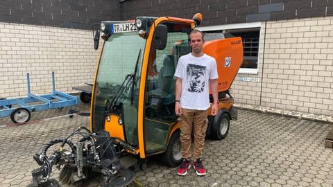 Patrick steht vor der Kehrmaschine auf dem Gelände der Lebenshilfe-Werke in Trier. Die Maschine durfte er schon oft fahren.  (Foto: SWR)