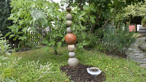 Upcycling im Garten: Eine alte Suppenschüssel mit Steinen darin dient als Tränke für Tiere. Auf einem Metallstab aufgereiht macht das Sammelsurium von unterschiedlichen Kugeln eine gute Figur. (Foto: SWR, Lara Bousch)