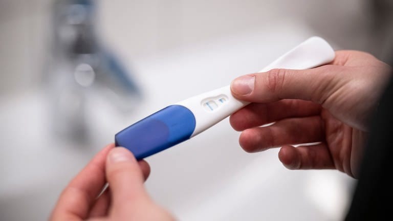 Eine Frau hält einen positiven Schwangerschaftstest in der Hand. Operative Schwangerschaftsabbrüche sind in Trier und Umgebung für Frauen nicht möglich. 