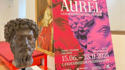 Eine Portraitbüste des römischen Kaisers Marc Aurel vor dem Plakat für die Landesausstellung 2025 in Trier (Foto: SWR)