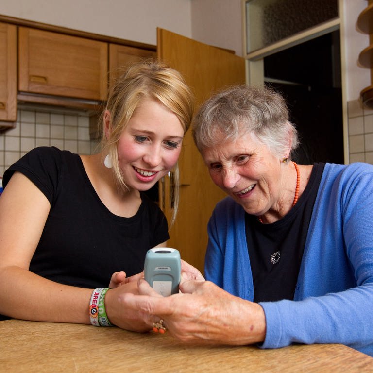 Pflegerin zeigt im Rahmen der ambulanten Pflege älterer Frau, wie ein Mobiltelefon funktioniert.