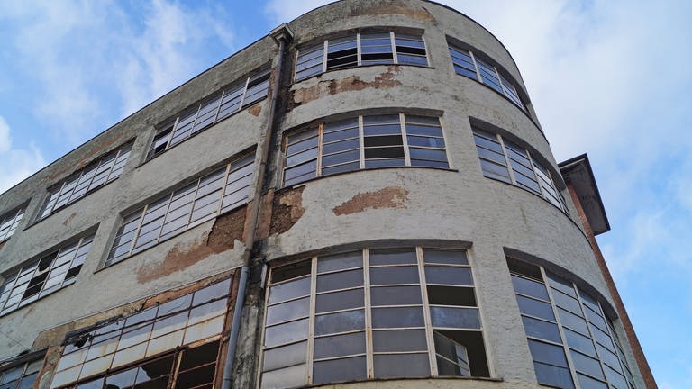Das Gebäude ist in keinem guten Zustand: Putz bröckelt von der Wand, Fensterscheiben sind eingeschlagen.