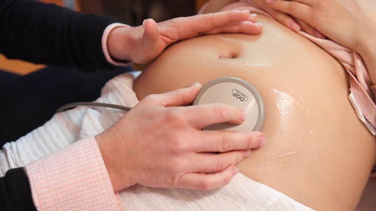 Eine Hebamme hört die Herztöne eines Babys im Mutterleib ab (Symbolbild)