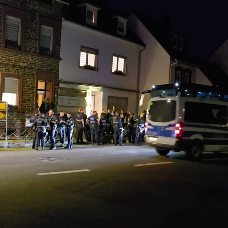 Eine Gruppe von Polizeibeamten steht vor einem Ferienhaus in Kröv an der Mosel. Dort lief ein Einsatz wegen des Verdachts der Verwendung verfassungsfeindlicher Parolen.