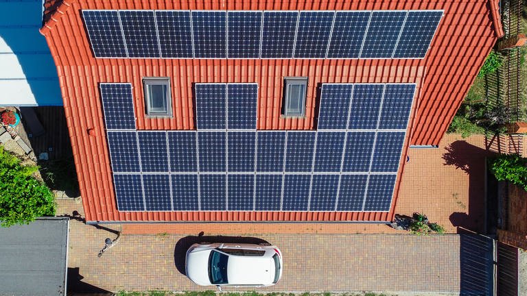 Eine Solaranlage auf einem Eigenheim (Luftaufnahme mit einer Drohne). Vor dem Haus steht ein Auto.