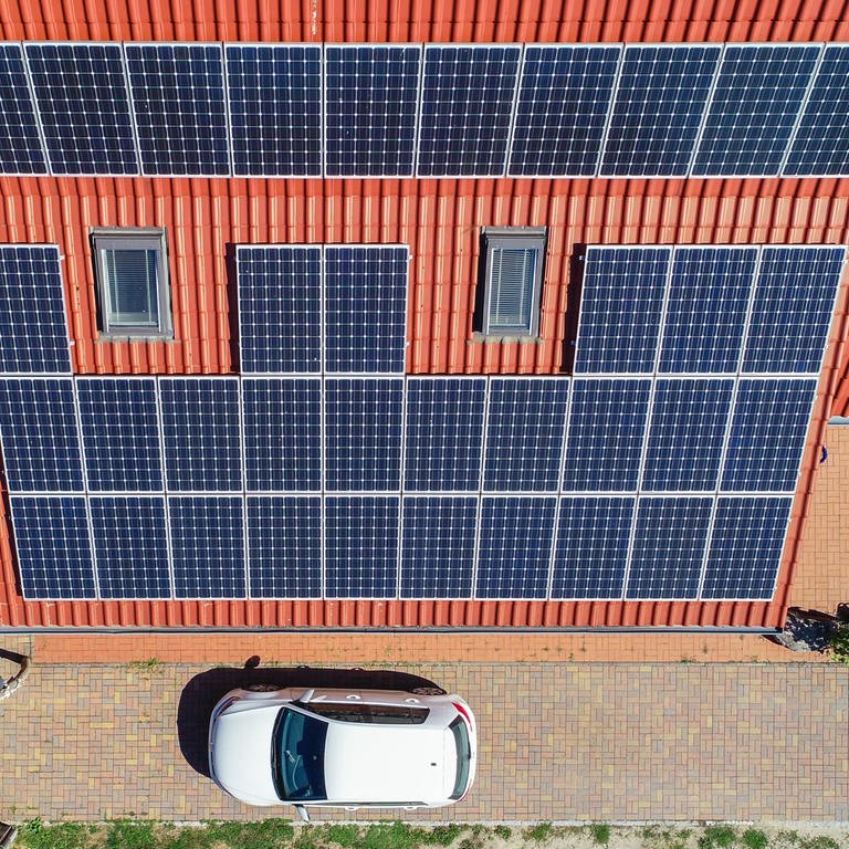 Eine Solaranlage auf einem Eigenheim (Luftaufnahme mit einer Drohne). Vor dem Haus steht ein Auto.