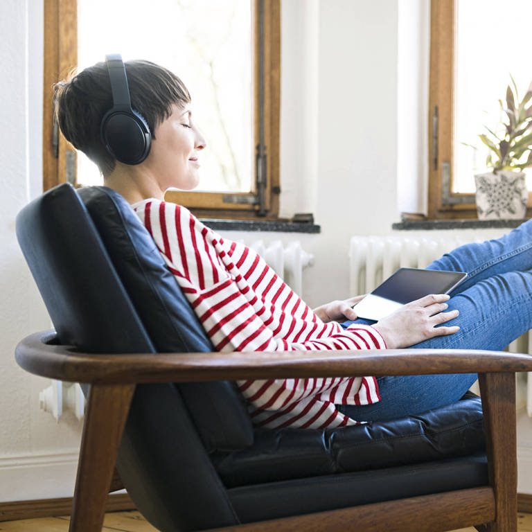 Frau mit aufgesetzten Kopfhörern in einem Sessel (Foto: IMAGO, Westend61)