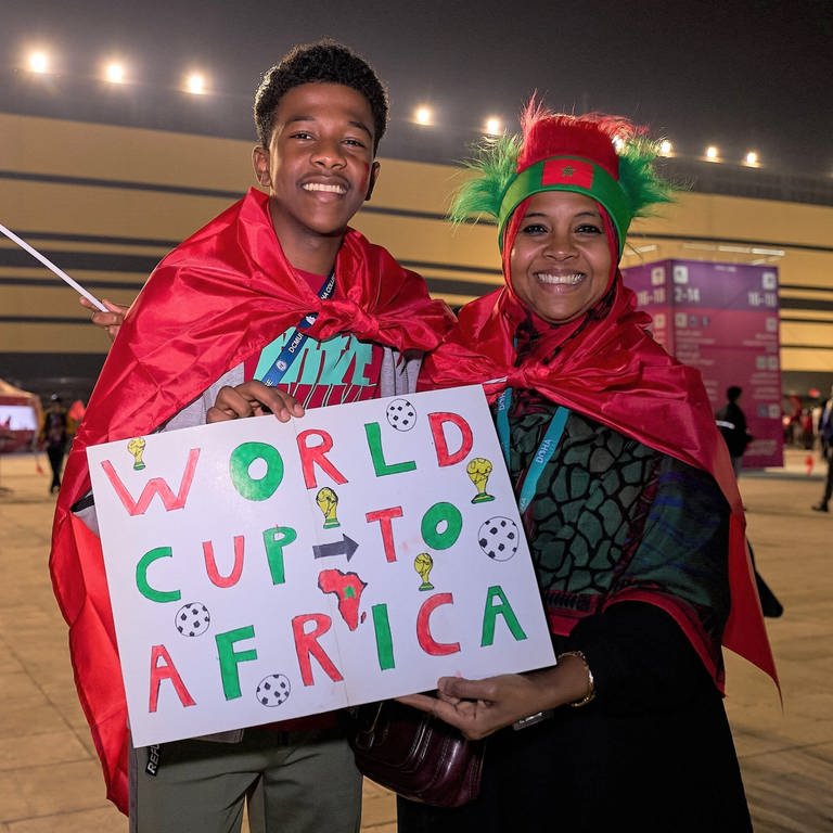 Zwei marokkanische Fans, ein junger Mann und eine Frau, halten ein Schild auf dem steht "World Cup to Africa"