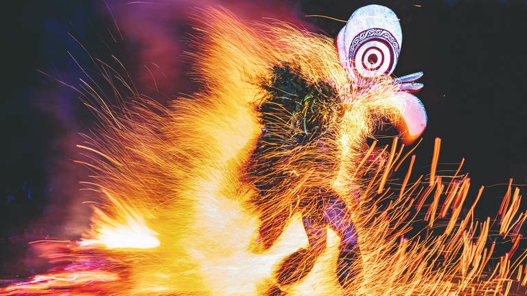 Tavurvur, Papua-Neuguinea – Beim Feuertanz, einem Ritual der Baining, tanzen maskierte Gestalten mit nackten Füßen durch das brennende Feuer. Dabei tragen die Männer, von denen keiner erfahren darf, wer es ist, eine Maske aus einem mit Rindenbast bezogenen Rattangestell. Über die traditionelle Bedeutung der Tänze spricht man kaum. (Foto: Pressestelle, © Ulla Lohmann/Knesebeck Verlag)