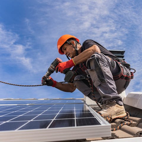 Symbolfoto: Techniker mit Bohrmaschine und Installation von Solarmodulen auf Dach (Foto: IMAGO, IMAGO / Westend61)