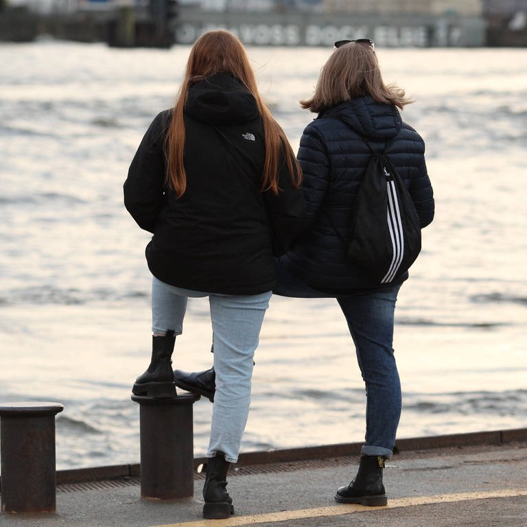 Freundinnen stehen an einer Hafenkante und schauen aufs Wasser