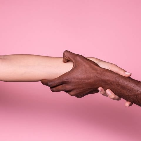 Ein schwarzer und ein weißer Arm reichen sich die Hand (Foto: IMAGO, IMAGO / Addictive Stock)