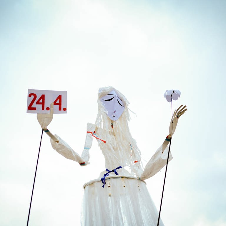 Eine große Marionette mit traurigem Blick, hält Schild mit dem Datum 24.4. in der rechten Hand (Foto: Pressestelle, Juliane Sauter)