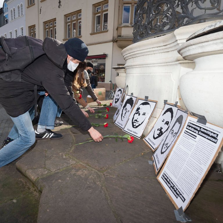 Mehrere Personen legen an  den Portraits der Ermordeten von Hanau rote Nelken nieder.  (Foto: IMAGO, BeckerBredel)