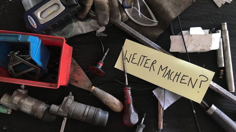 Verschiedene Werkzeuge und Rohrteile und ein Zettel auf dem "Weitermachen? steht (Foto: SWR, Foto: Lisa Spöri)