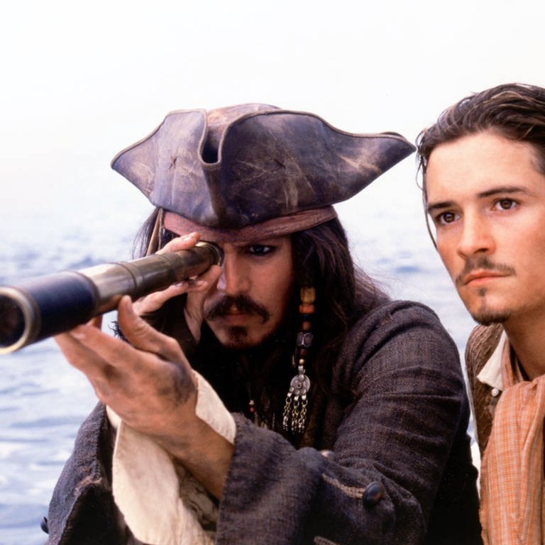 Johnny Depp schaut als Captain Jack Sparrow durch ein Fernglas. Neben ihm Orlando Bloom. (Foto: dpa Bildfunk, picture-alliance / Mary Evans Picture Library)