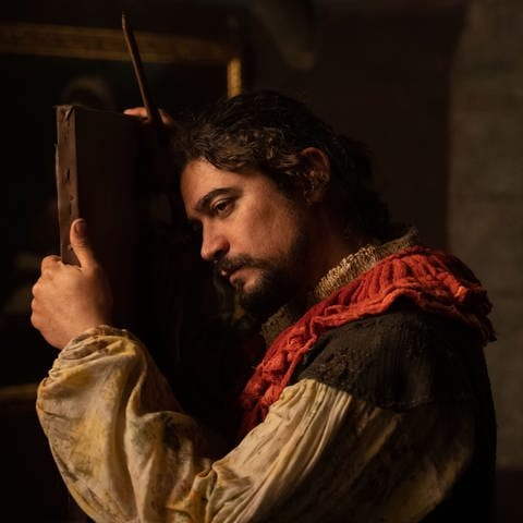 Szene aus dem Film "Der Schatten von Caravaggio": Riccardo Scamarcio in der Rolle des Caravaggio lehnt an Staffelei