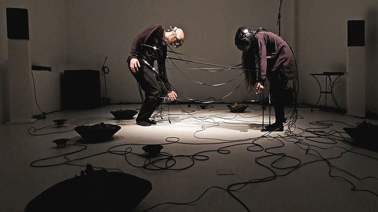 zwei Menschen, gebückt, mit Kabeln verbunden