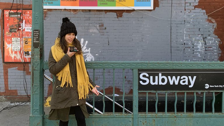 eine junge Frau vor einer Subway-Statuion spricht in ihr Handy - Produktionsfoto "Re:Produktion"