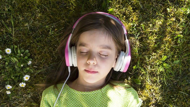 Mädchen mit Kopfhörern liegt auf einer Wiese (Foto: IMAGO, imago images / Westend61)