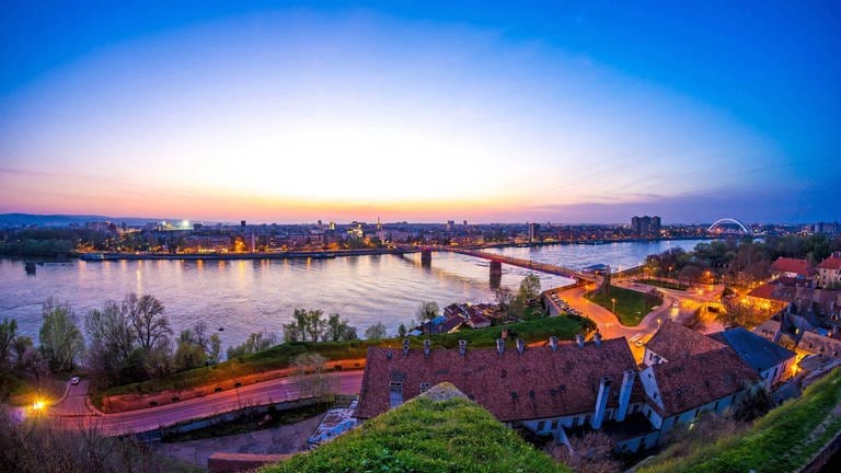Als Brückenbauer sieht Novi Sad, die Hauptstadt der serbischen Vojvodina, seine Rolle als europäische Kulturhauptstadt. Der EU-Beitrittskandidat setzt auf große Events: Blick in der Dämmerung auf die Donau, Brücke und Stadt Novi Sad. (Foto: IMAGO, IMAGO / Shotshop)