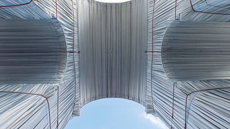 Blick von unten: Der Faltenwurf und die Kontur-gebenden Schnürungen wurden von Christo genau geplant: Blick von unten auf den verhüllten Arc de Triomphe, man sieht die silber-blauen Stoffe und rote Befestigungsseile.