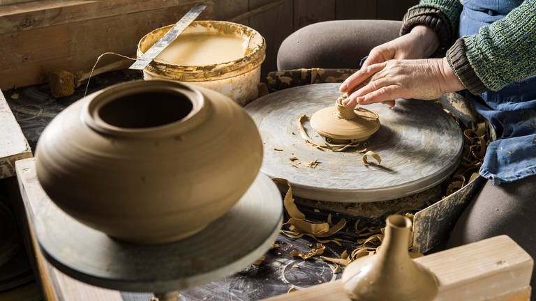 Keramikwerkstatt, Hände formen Deckel der Kanne mit Modellierschlinge auf Drehscheibe