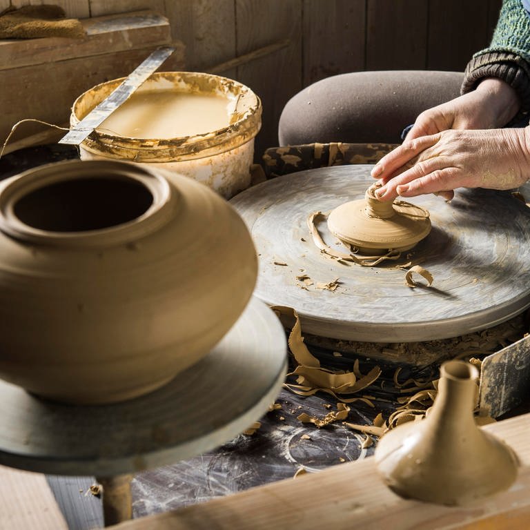 Keramikwerkstatt, Hände formen Deckel der Kanne mit Modellierschlinge auf Drehscheibe